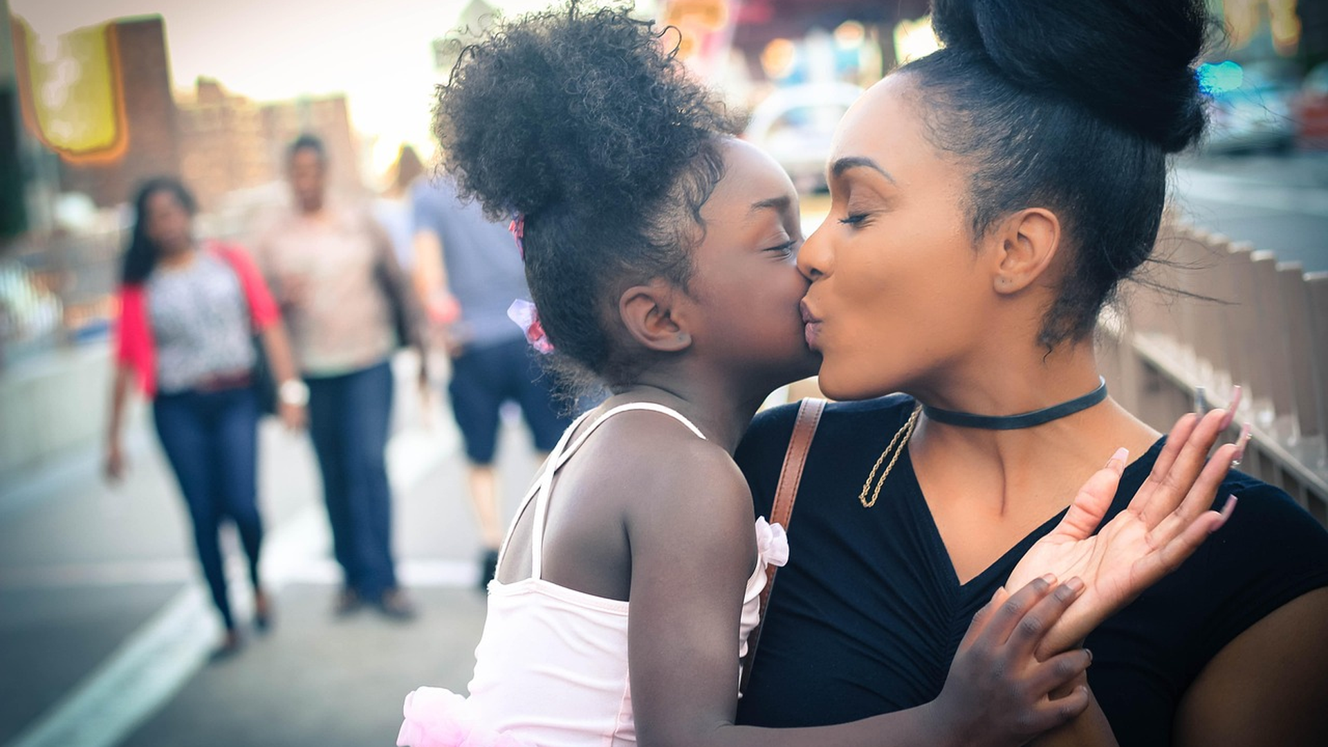 African American mother holding her young daughter with textured curly hair in a US city neighborhood