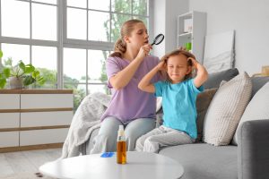Mother using a magnifier to examine her young daughter's scalp for head lice and nits at home under good light