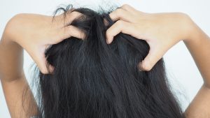 A mother carefully parts and examines her young daughter's hair indoors after an at-home lice treatment, checking the scalp for signs of irritation or remaining nits.