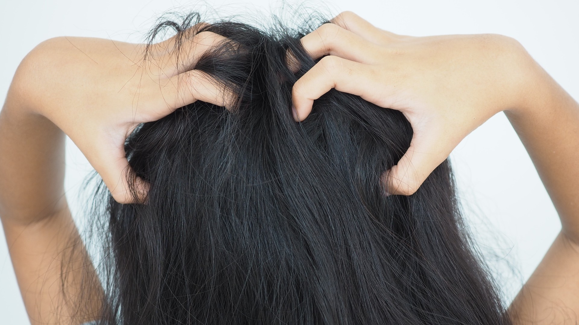 A mother carefully parts and examines her young daughter's hair indoors after an at-home lice treatment, checking the scalp for signs of irritation or remaining nits.