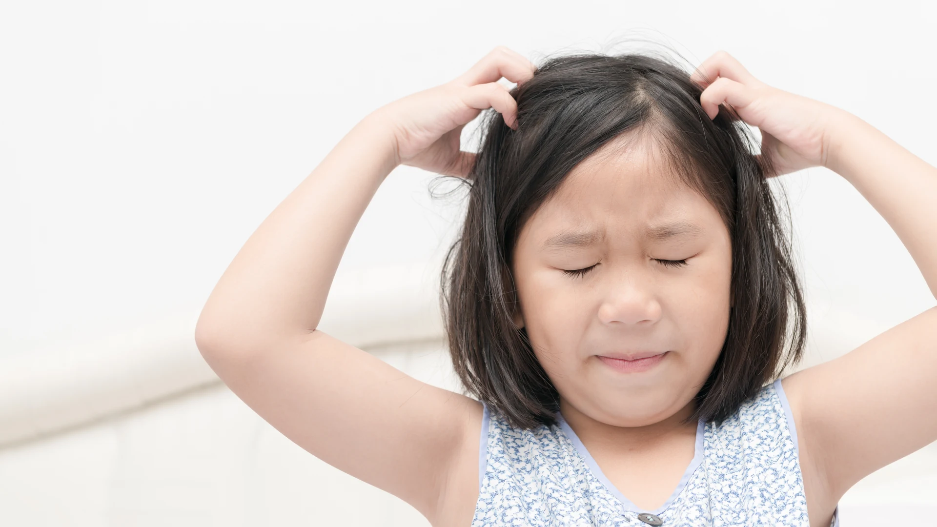 Child scratching her scalp, a common sign that may indicate head lice