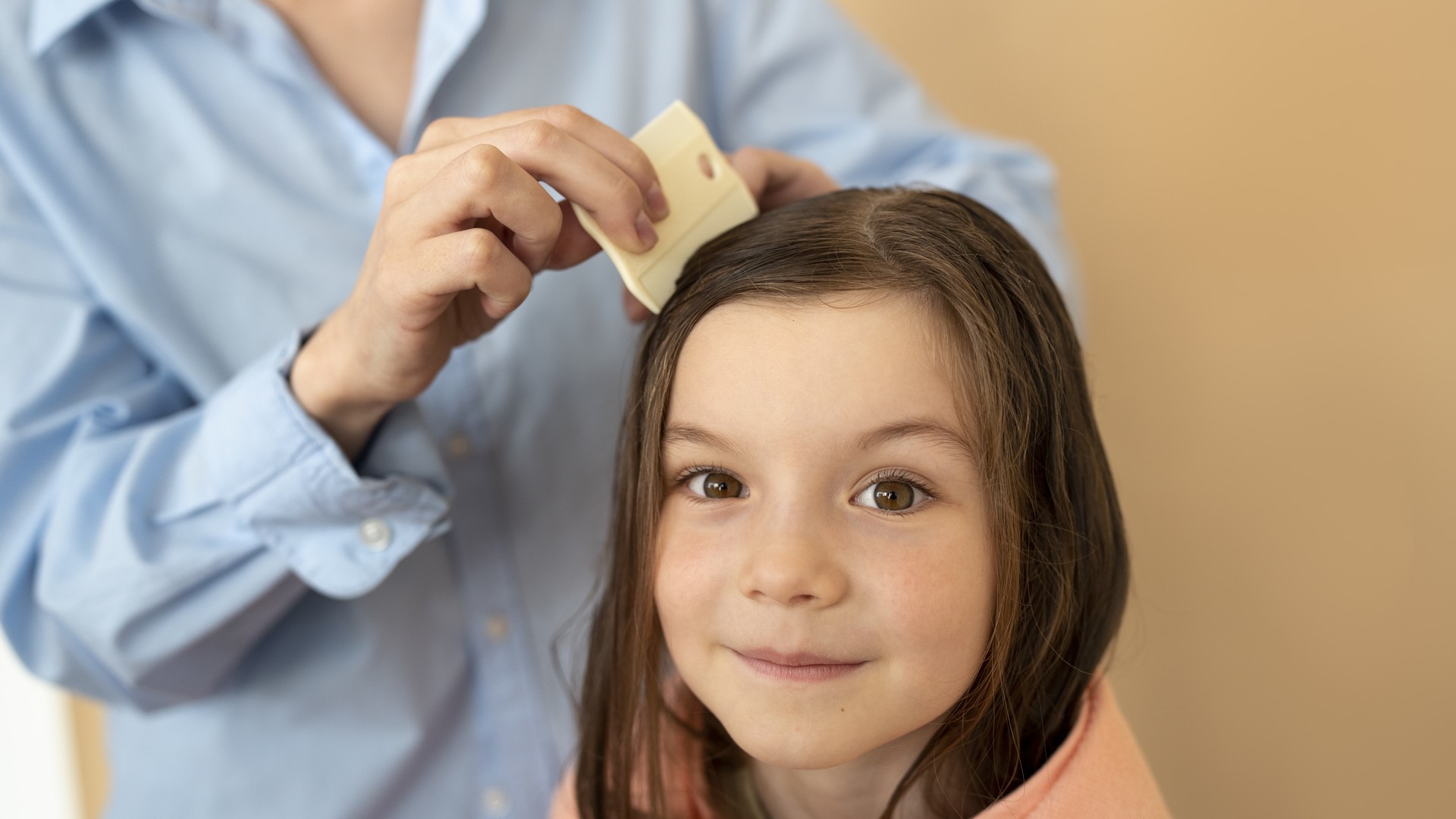 A parent parting a child's hair to check the scalp for live lice a week after treatment