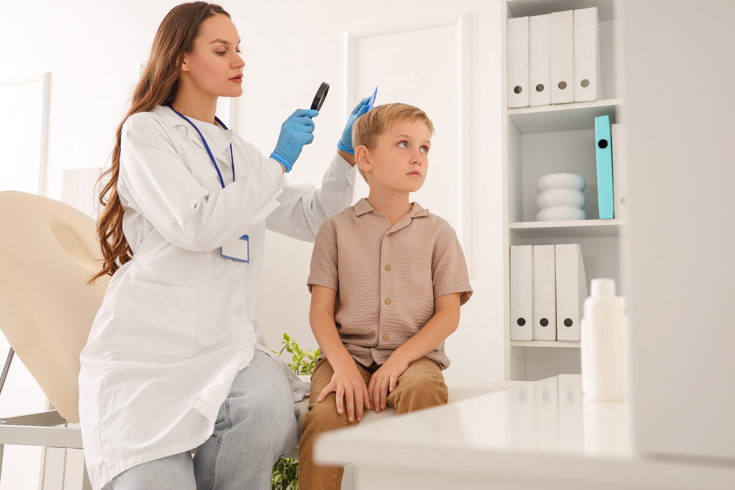 Clinician using a magnifier and lice comb to check a young boy's scalp in a clinic