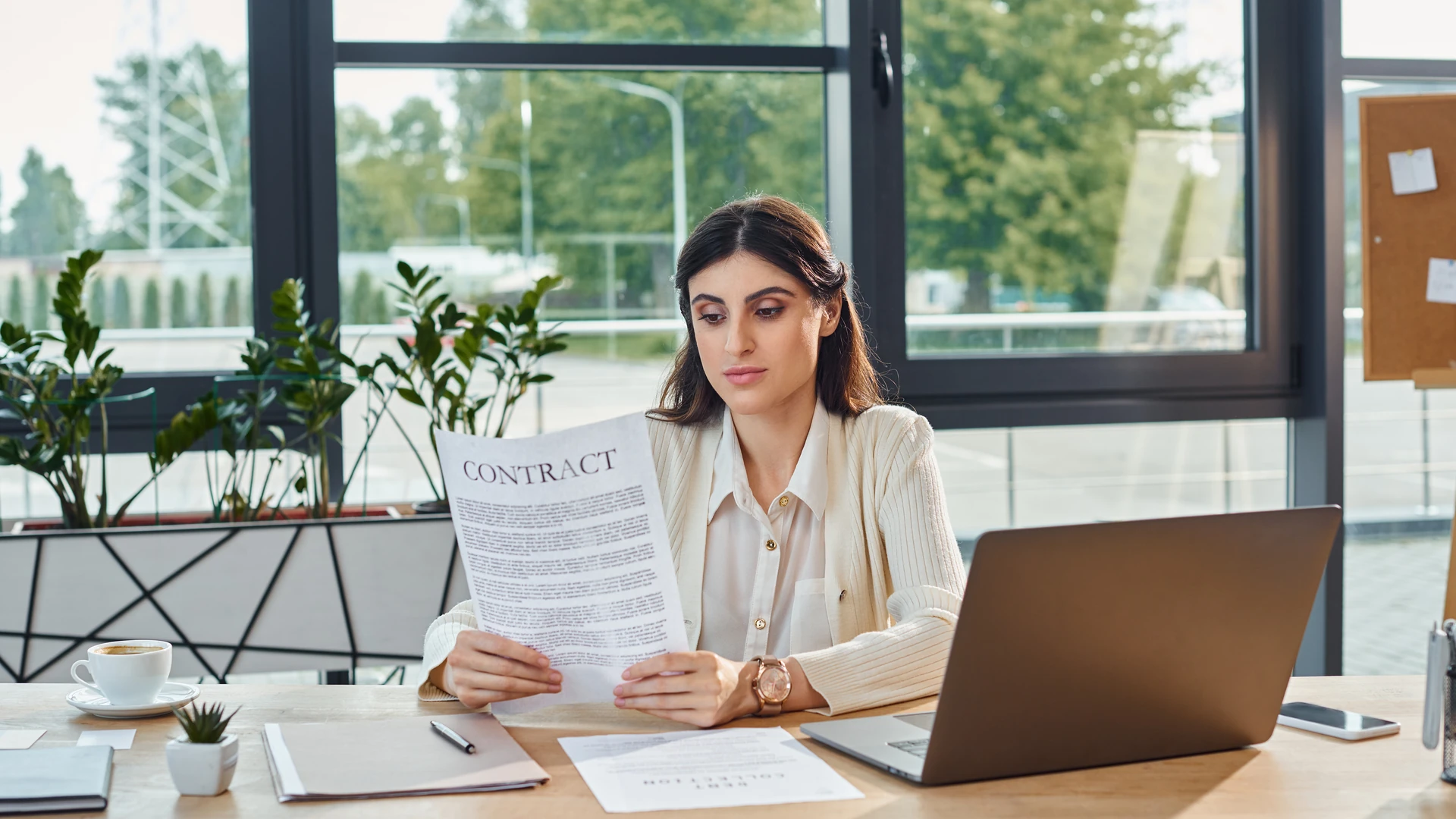 Businesswoman at a desk with a laptop reading a printed contract